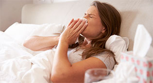 A woman in bed blowing her nose surrounded by tissues